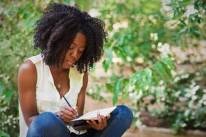 Closeup portrait of young attractive black woman working, making notes and sitting in park