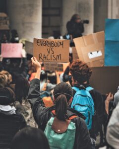 People at a demonstration with one person holding a sign on card that says 'everybody vs racism.'
